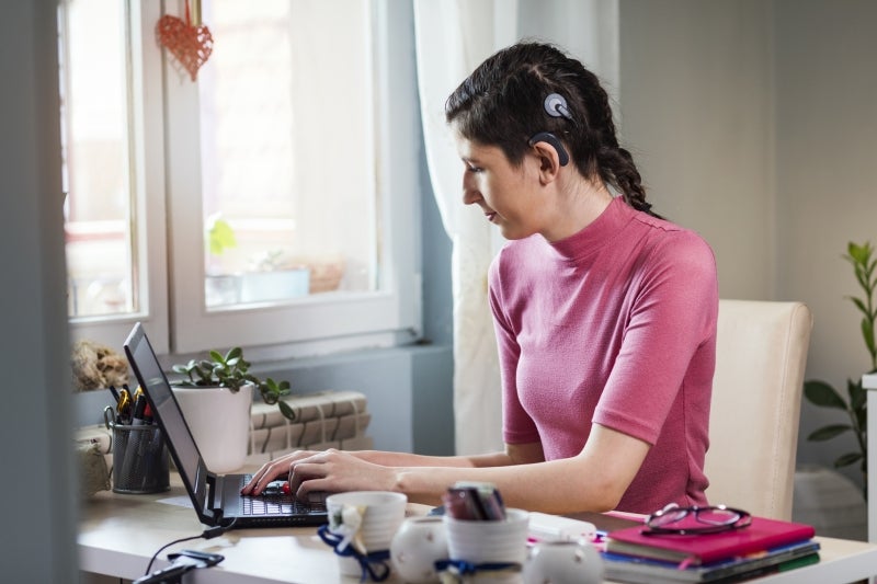 Woman working on computer utilizing cochlear implant