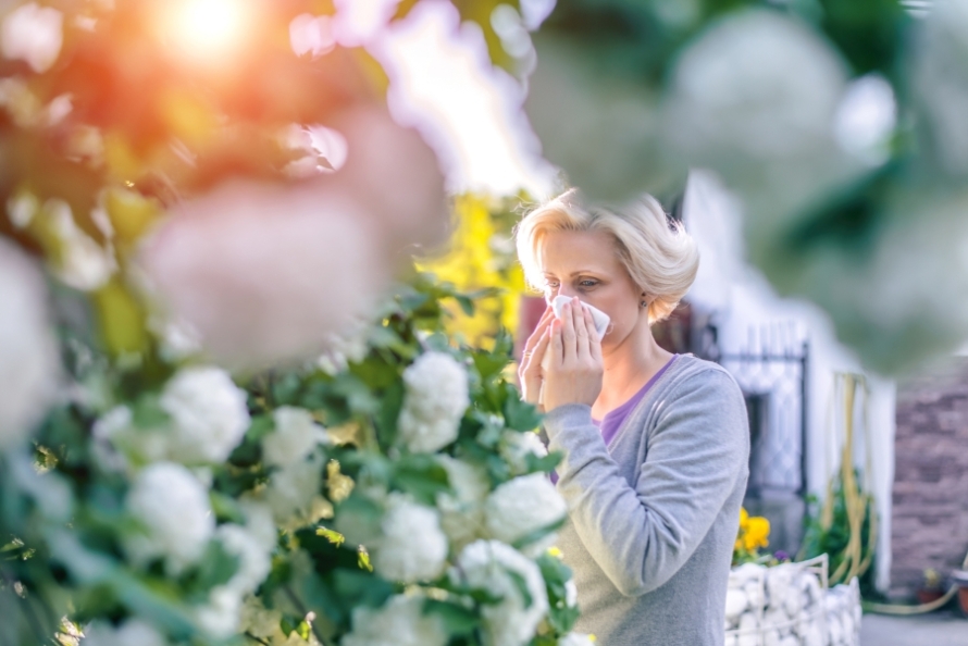 Image of woman reacting to seasonal pollen by sneezing